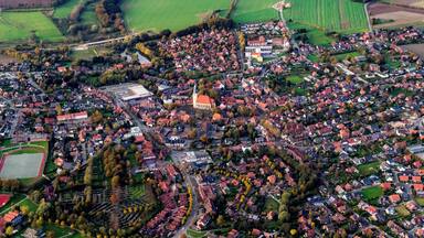 Une vue aérienne d’une ville avec des maisons aux toits rouges, des champs verdoyants et une église centrale.