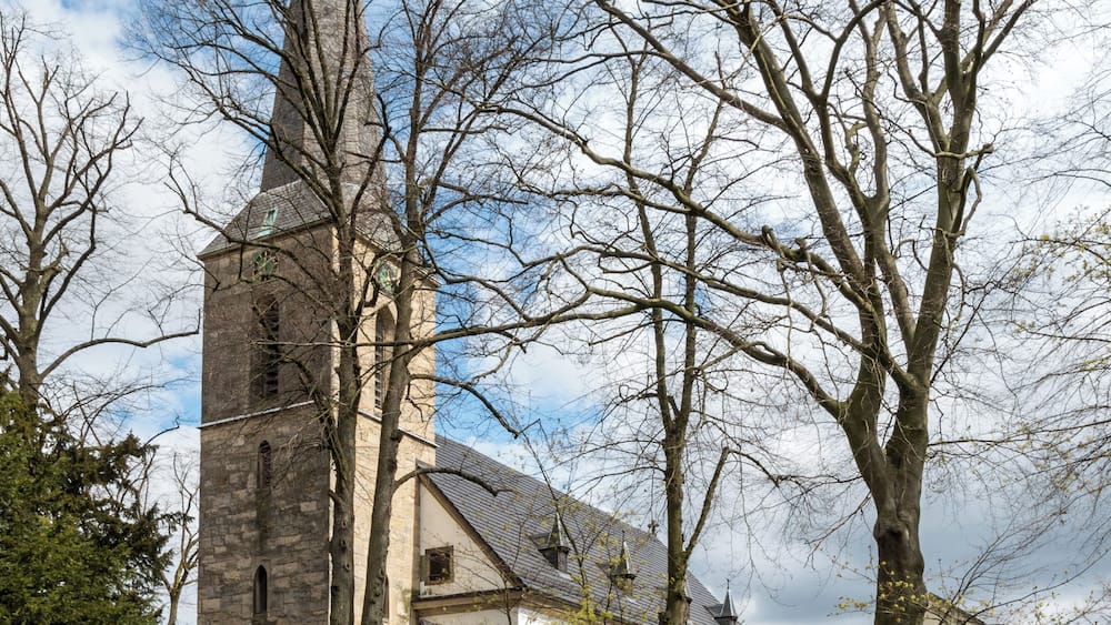 A church with a tall spire, surrounded by trees and a brick pathway.