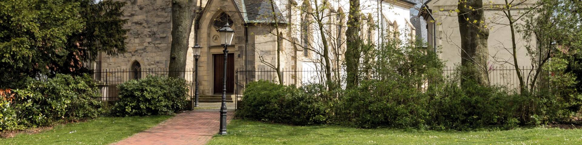 A church with a tall spire, surrounded by trees and a brick pathway.