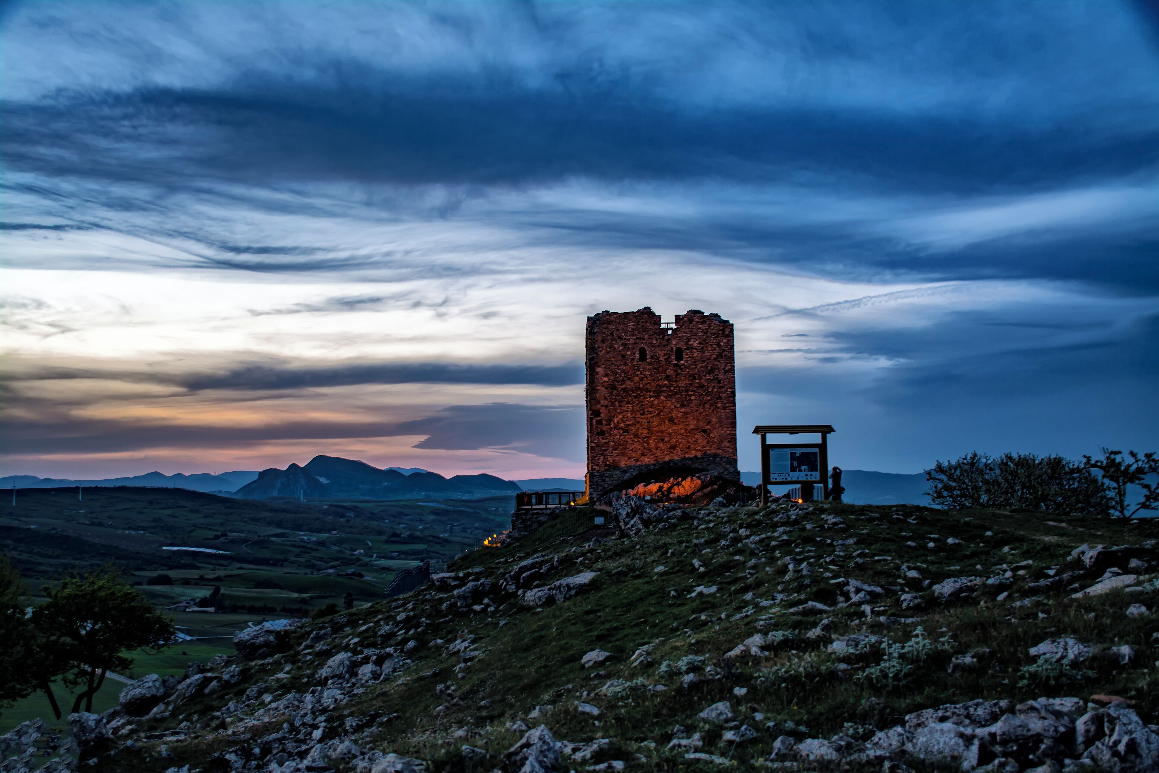 A stone tower on a hill with a sunset in the background.