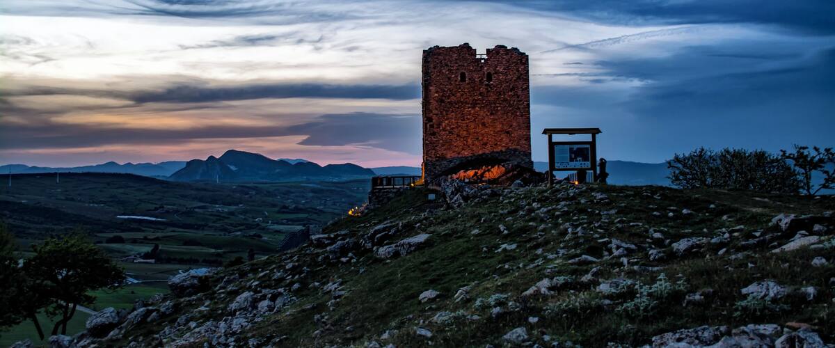 A stone tower on a hill with a sunset in the background.