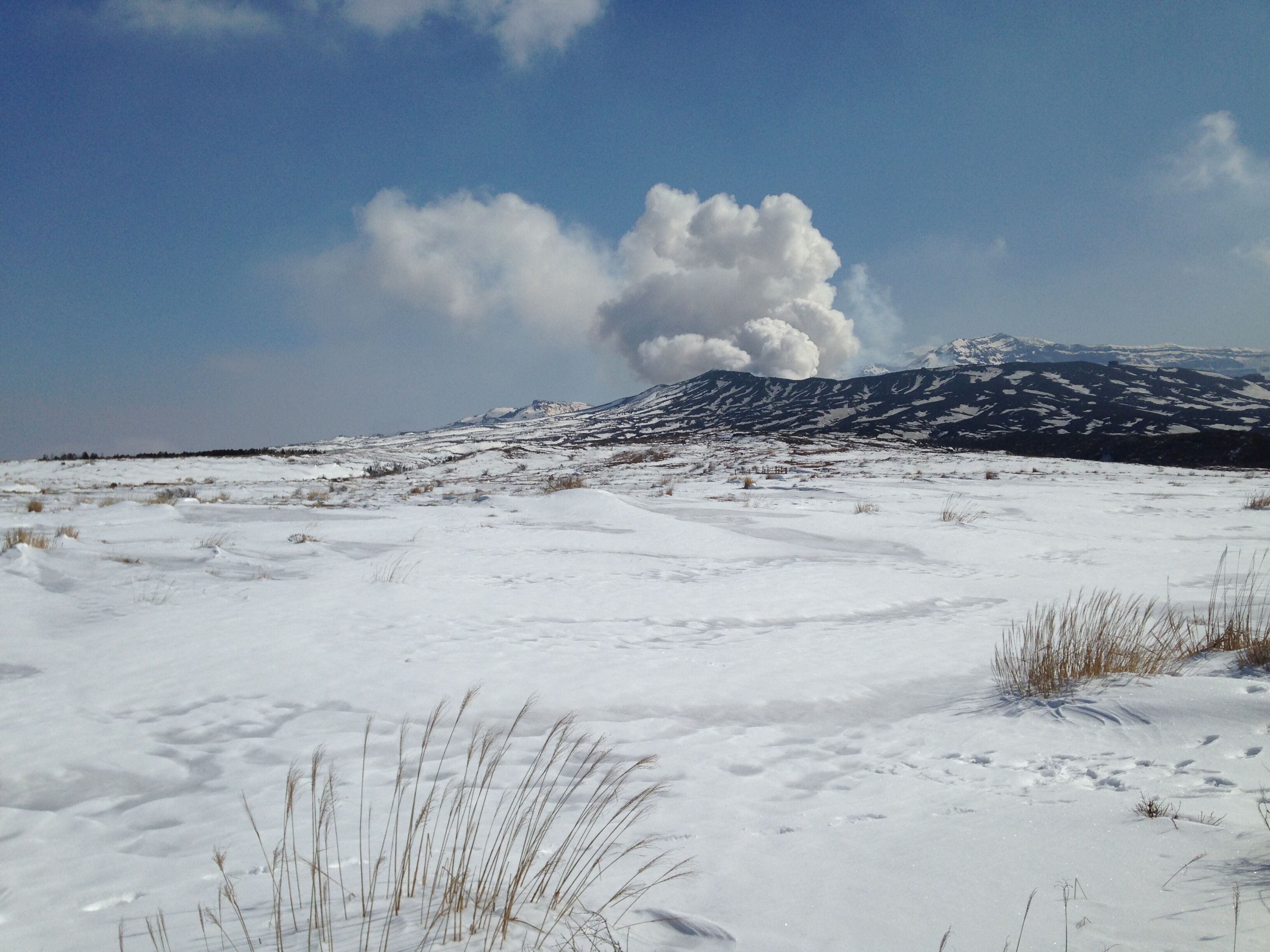 A snowy landscape with a mountain in the background and a large cloud formation.