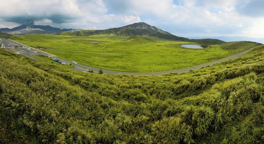 Un camino sinuoso atraviesa un valle verde exuberante, con un lago y una montaña al fondo.