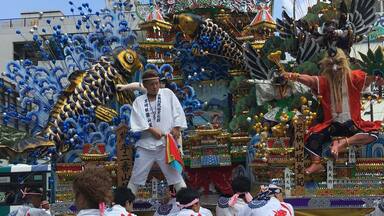 A parade with participants in traditional white attire, carrying a large ornate float with colorful decorations and figures.