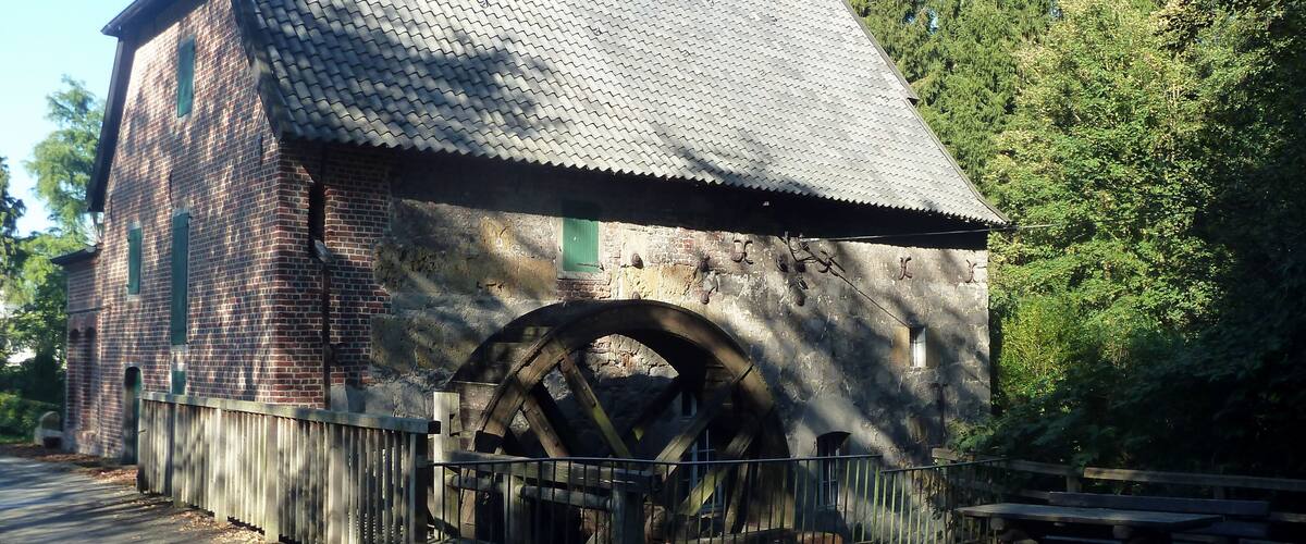 A historic brick building with a large water wheel and a wooden fence.