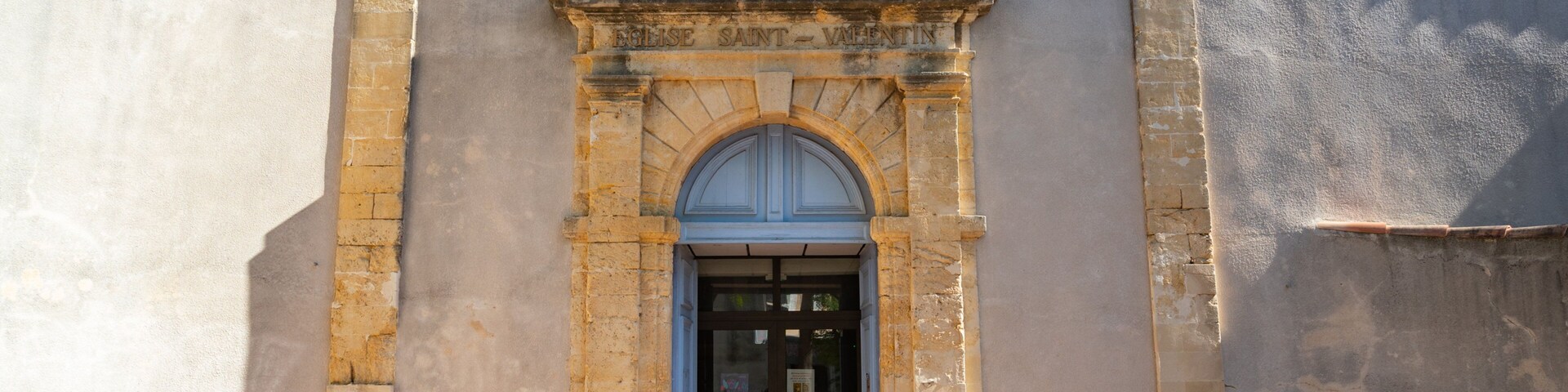 L’entrée d’une église, avec une porte bleue et une statue au-dessus.
