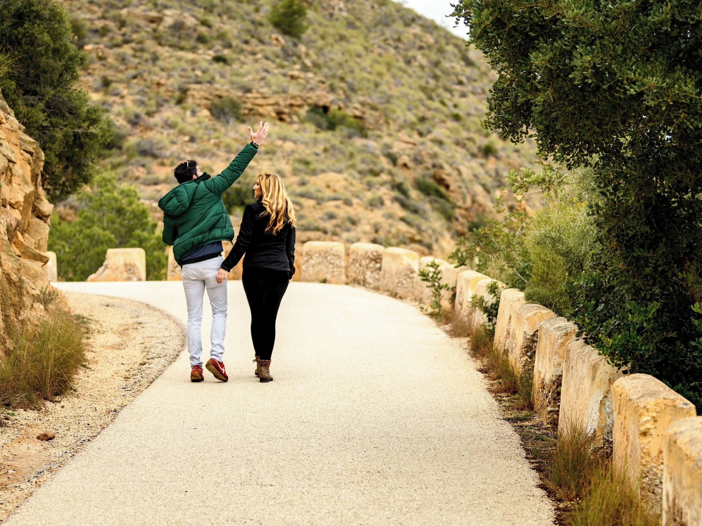 A couple walking on a paved road surrounded by stone walls and greenery.