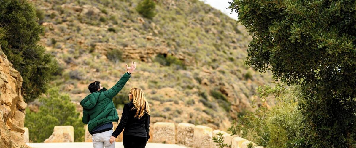 A couple walking on a paved road surrounded by stone walls and greenery.