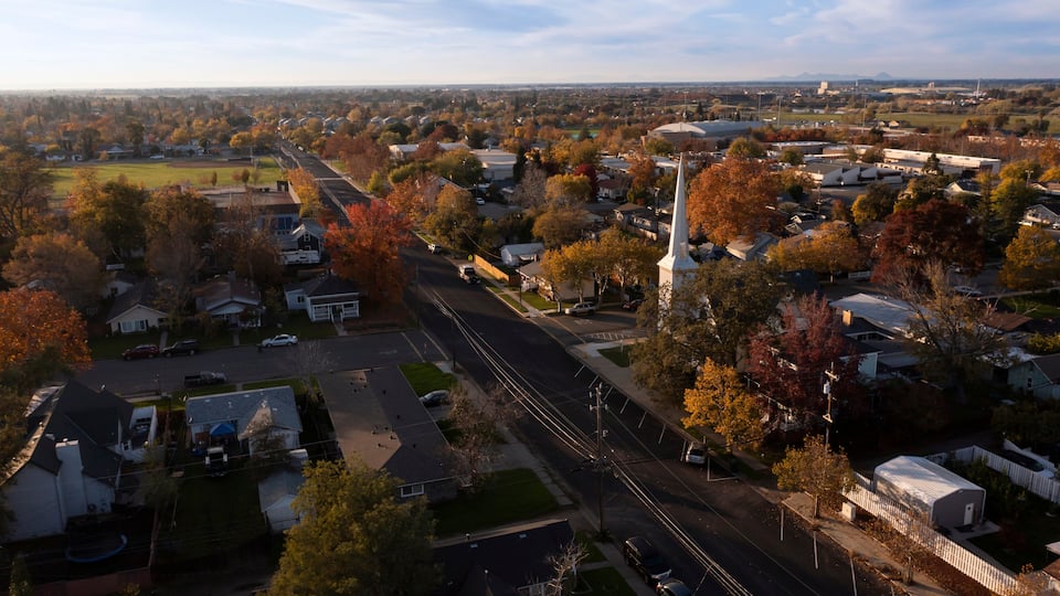 An aerial view of a suburban area with autumn-colored trees, a prominent church steeple, and a mix of residential and commercial buildings.