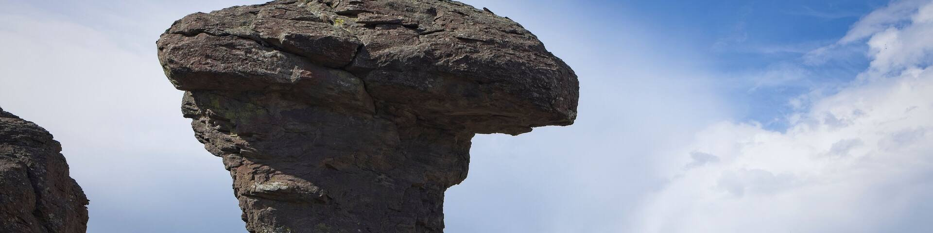 A rock formation with a prominent overhang in a desert landscape.