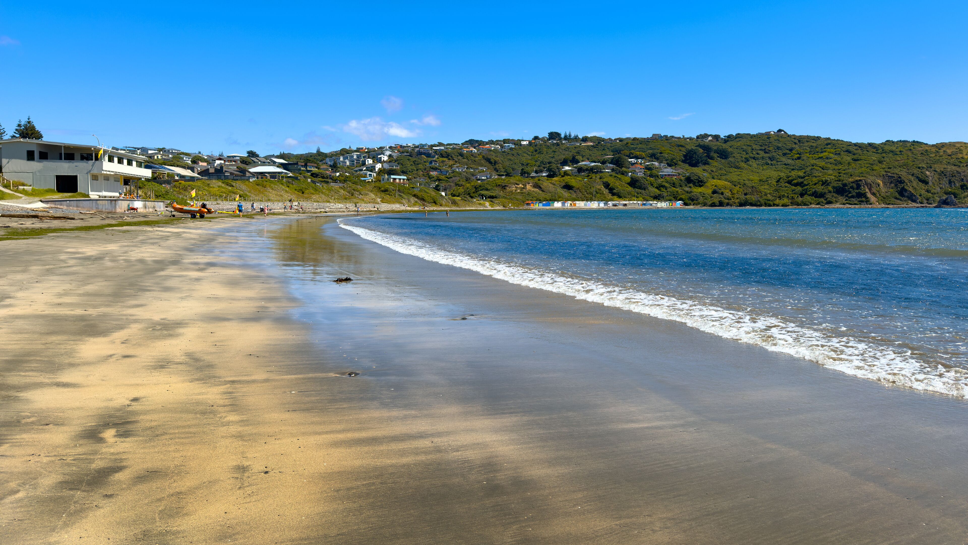 Tītahi Bay beach, Porirua, Wellington, New Zealand. Surf Life Saving Club at left, boatsheds and houses in distance. Panoramic view.