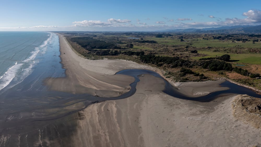 A coastal landscape with a sandy beach, a river, and distant mountains.
