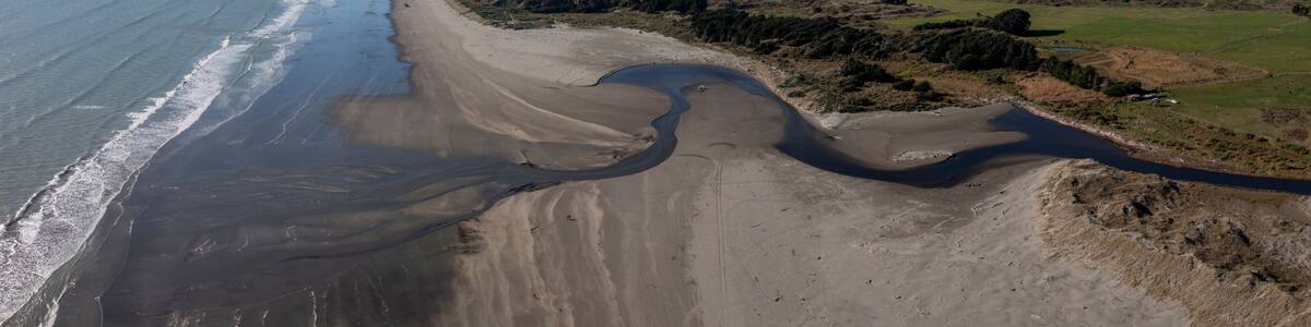 A coastal landscape with a sandy beach, a river, and distant mountains.