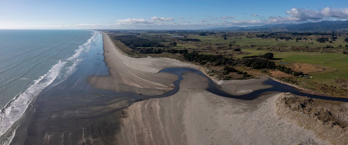 A coastal landscape with a sandy beach, a river, and distant mountains.