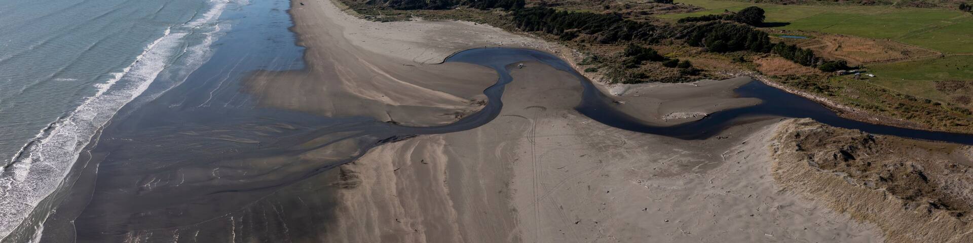 A coastal landscape with a sandy beach, a river, and distant mountains.