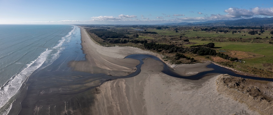Un paisaje costero con una playa arenosa, un río y montañas a lo lejos.