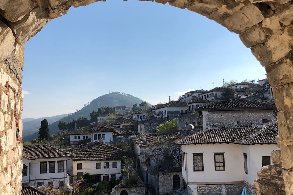 A stone archway framing a view of a hillside village with traditional buildings and a narrow street.