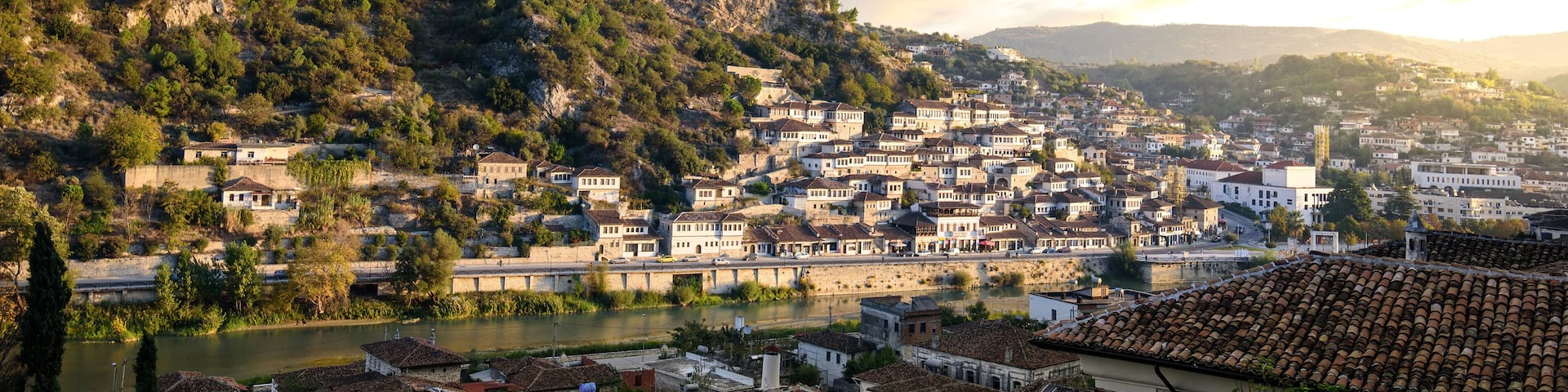 A town nestled between hills with a river, historic buildings, and a flag on a hilltop.
