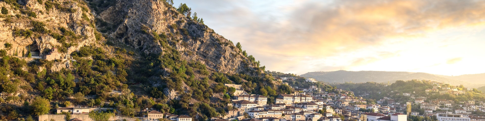 A town nestled between hills with a river, historic buildings, and a flag on a hilltop.