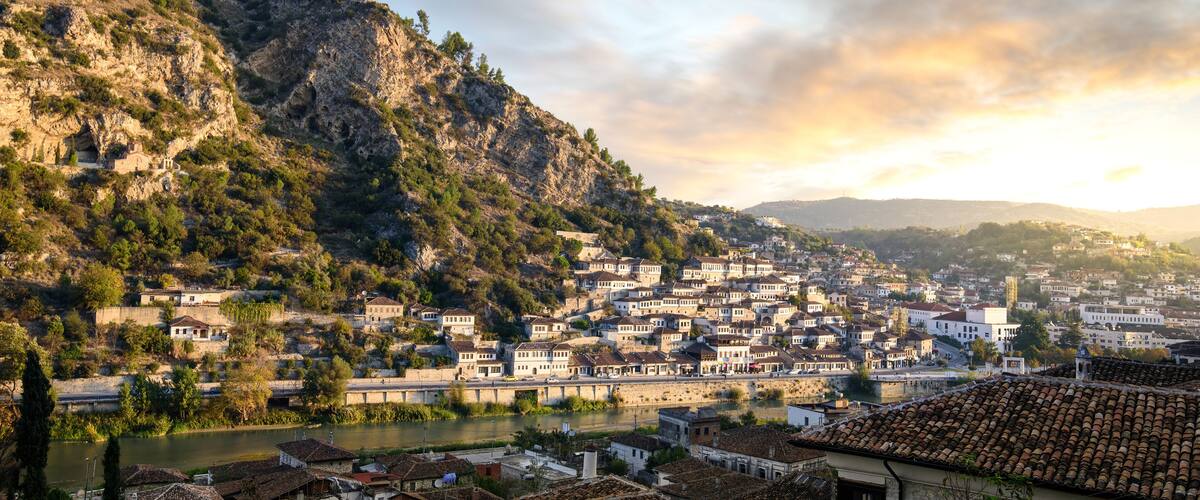 A town nestled between hills with a river, historic buildings, and a flag on a hilltop.