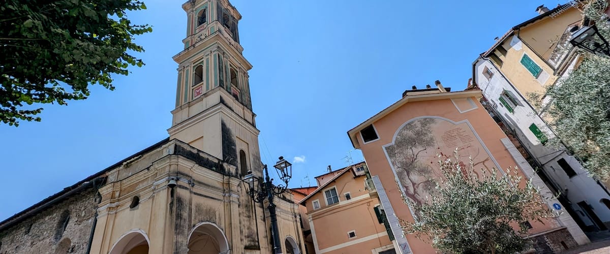 A historic church with a tall bell tower, arched doorways, and a mural on a nearby building.