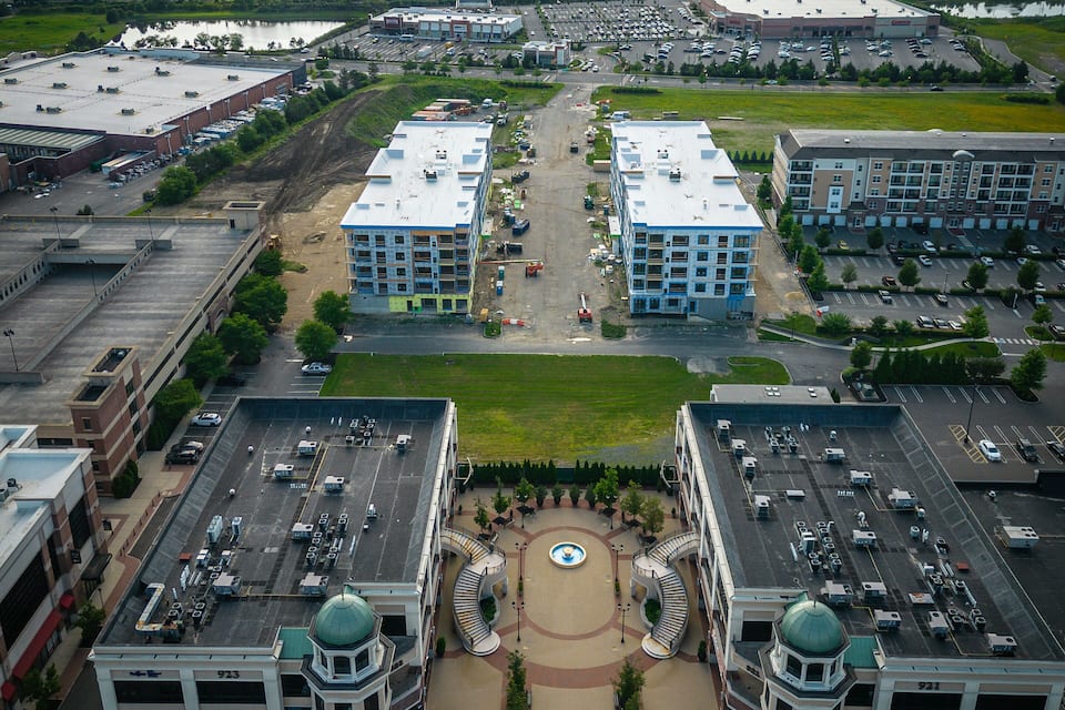 An aerial view of a cityscape with two prominent blue-roofed buildings, a parking lot, and a distant skyline.