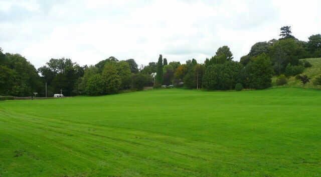 A large green field with trees and a hill in the background.