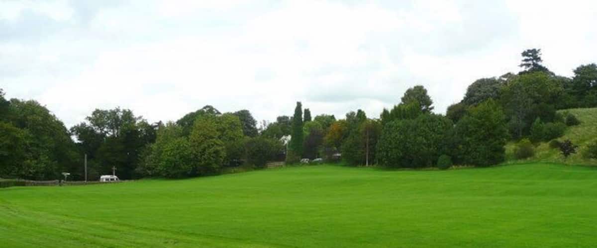 A large green field with trees and a hill in the background.