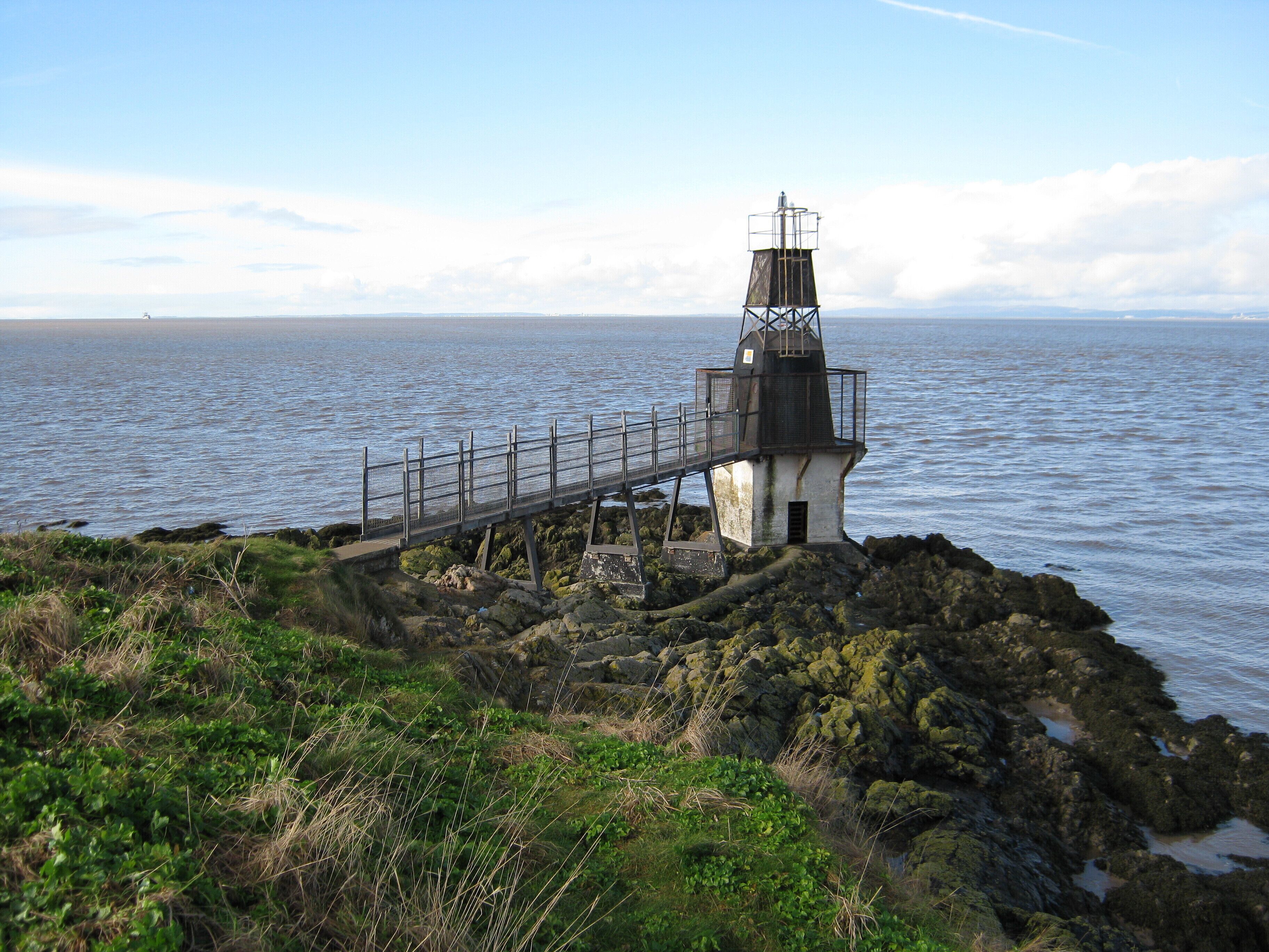 A lighthouse on a rocky outcrop with a metal walkway leading to it.
