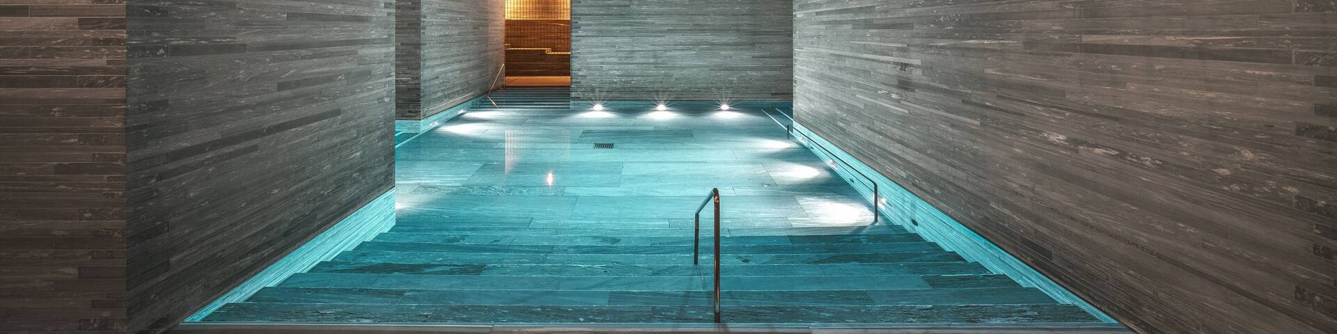 A modern indoor swimming pool with wooden walls and a central light source.
