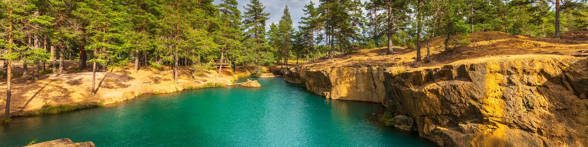 View of Ostra Silvberg gruva, a turquoise lake in a former mine surrounded by rocky cliffs and pine trees in Borlange, Dalarna County, Sweden.