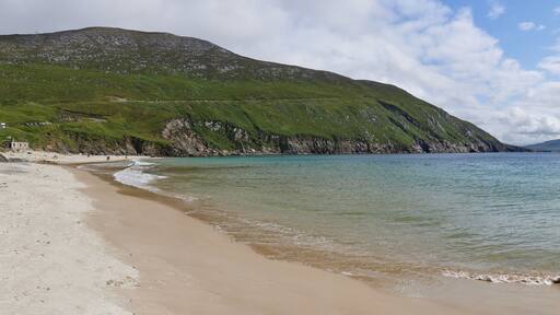 A beach with clear turquoise waters, green hills, and a distant mountain range.