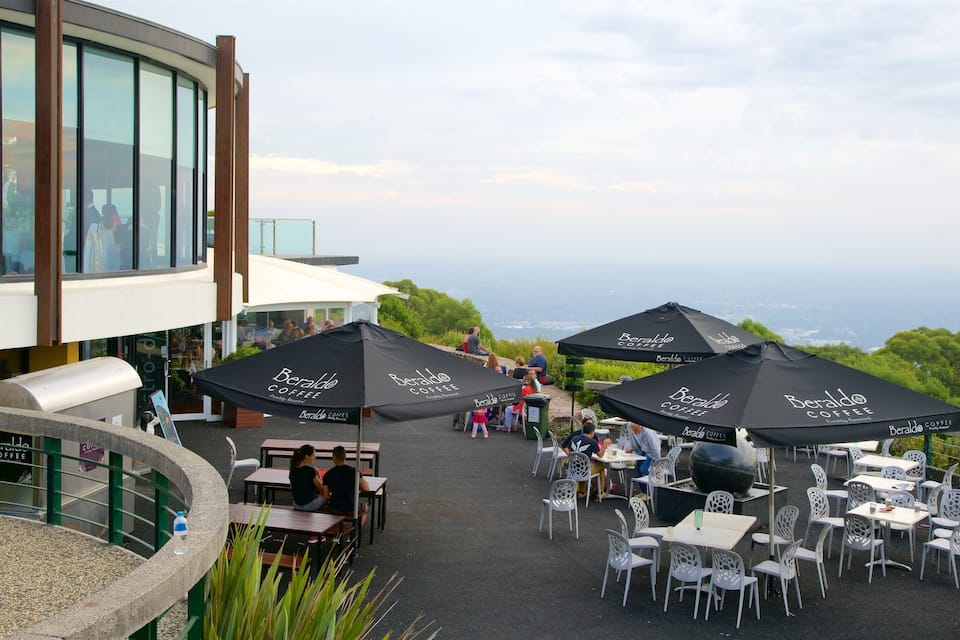 An outdoor café with tables and chairs, black umbrellas, and a view of the sea.