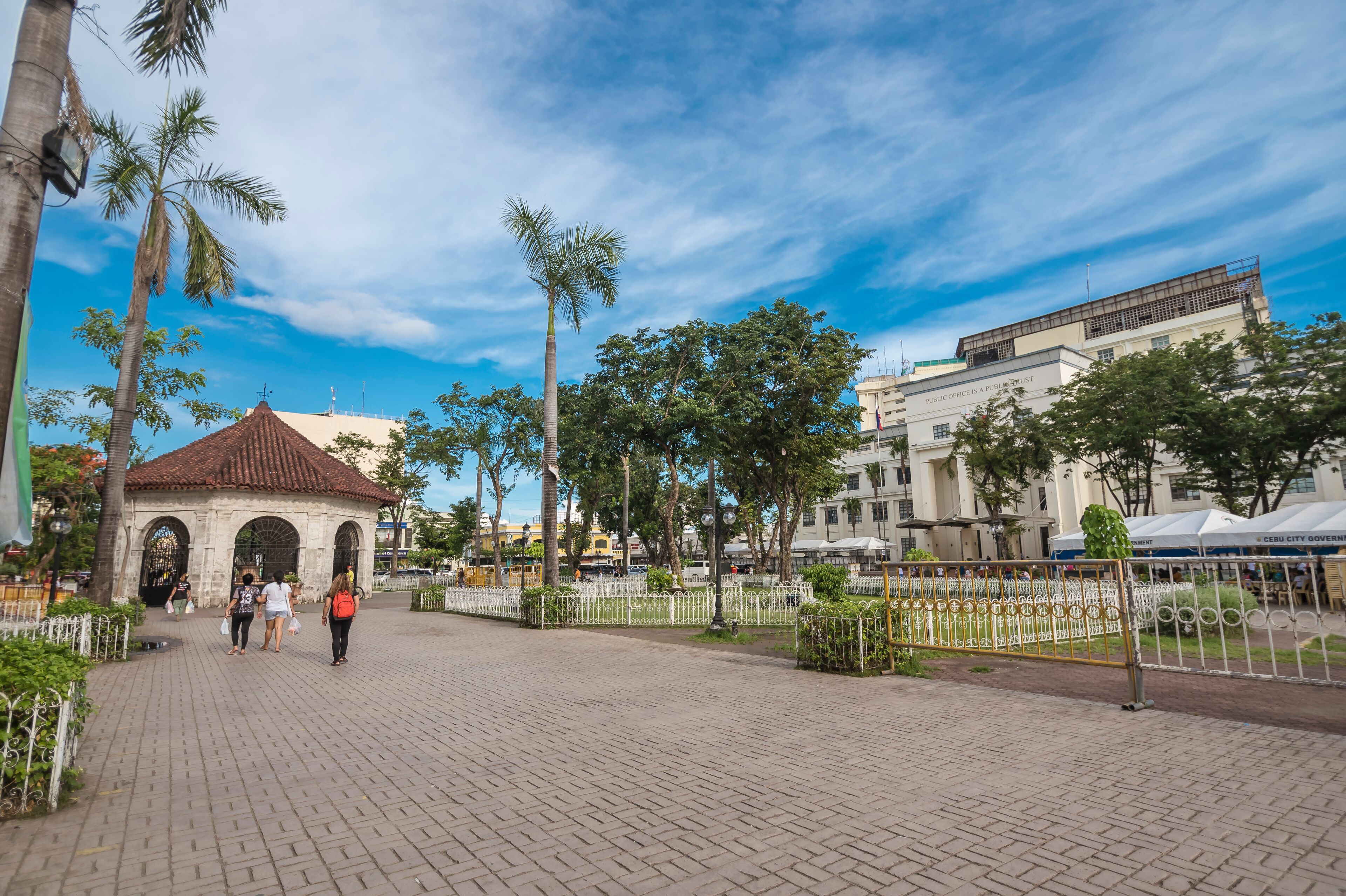 A paved plaza with a gazebo, palm trees, and a building with a sign reading "Public Office".