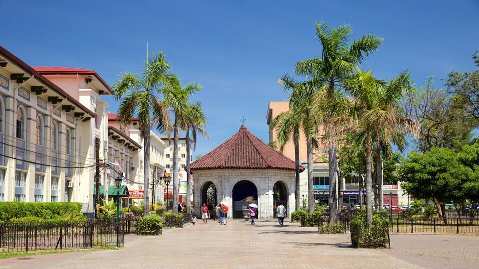 A plaza with a central archway, palm trees, and buildings with commercial signs.