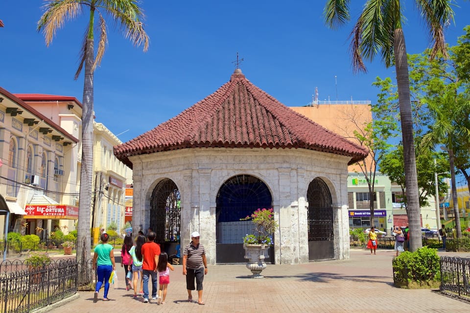 A traditional stone archway with a tiled roof, surrounded by palm trees and modern buildings.