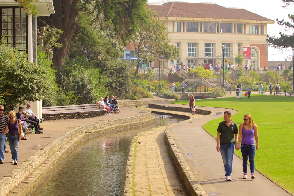 Un parc amb un canal d'aigua, bancs i gent passejant.
