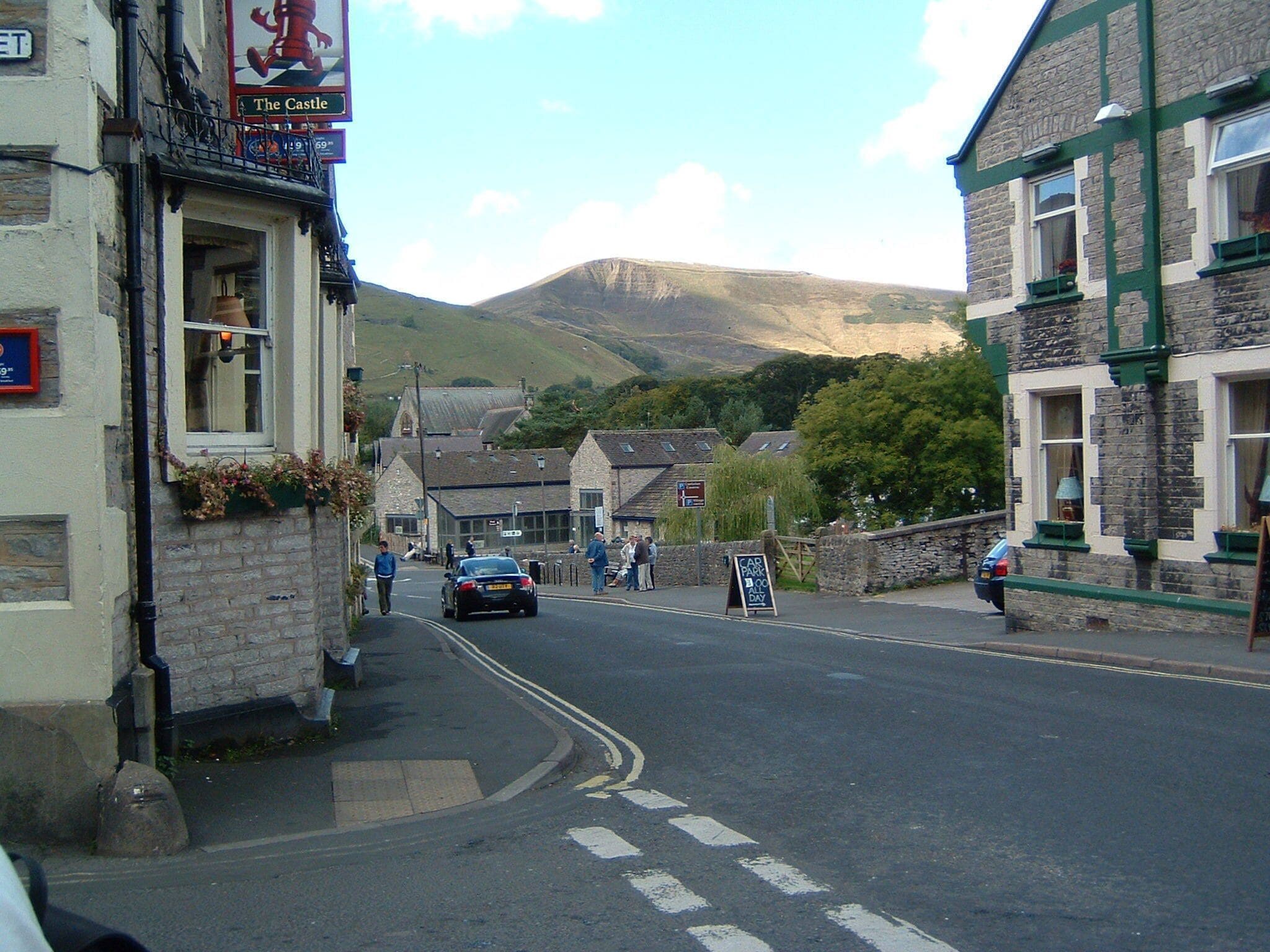 A street with buildings, a sign for 'The Castle', and a car parked on the side.