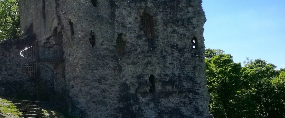 Un castillo en ruinas con una escalera que lleva hasta él, rodeado de vegetación.