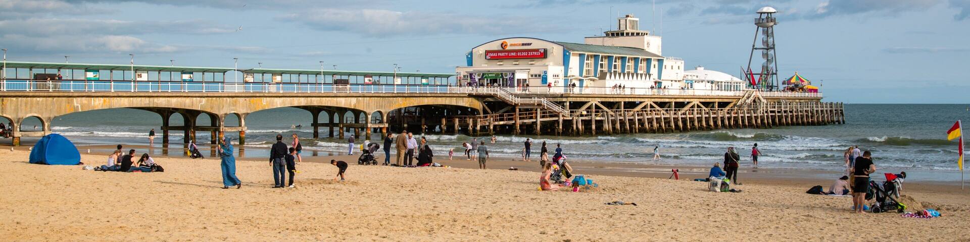 A beach with a pier, a lighthouse, and a building with a Christmas party sign.