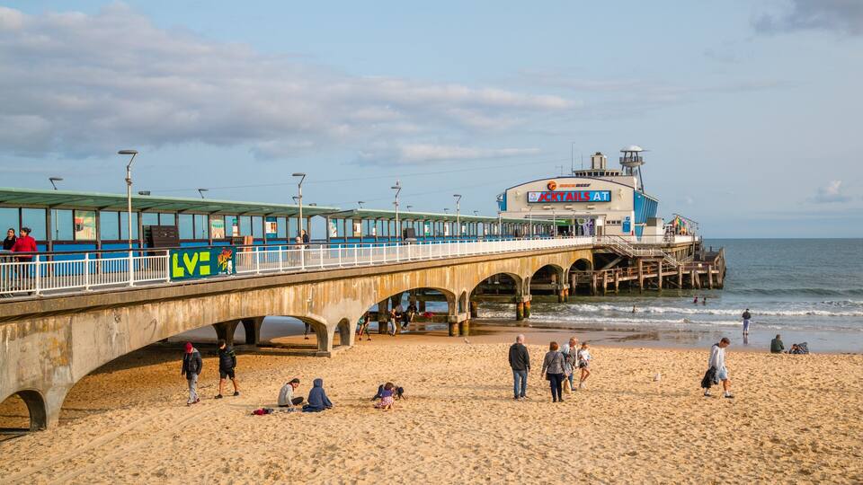 A pier with a restaurant named "JACKTAILS AT" and a beach with people walking and children playing.