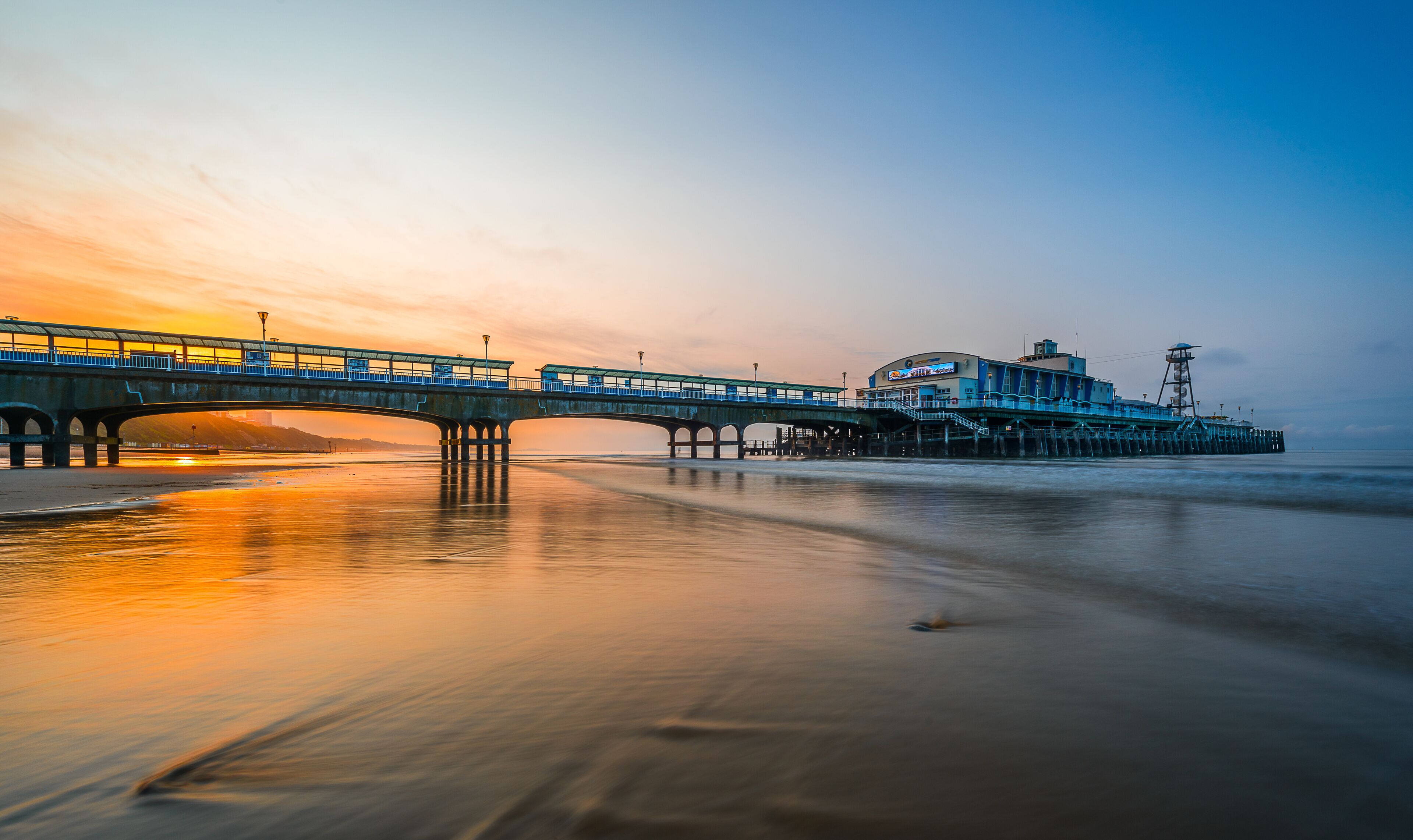 A bridge over a calm body of water at sunset with a pier extending into the water.
