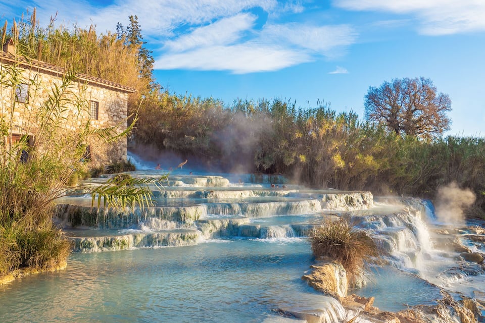 A stone building, terraced hot springs, and a forested area.