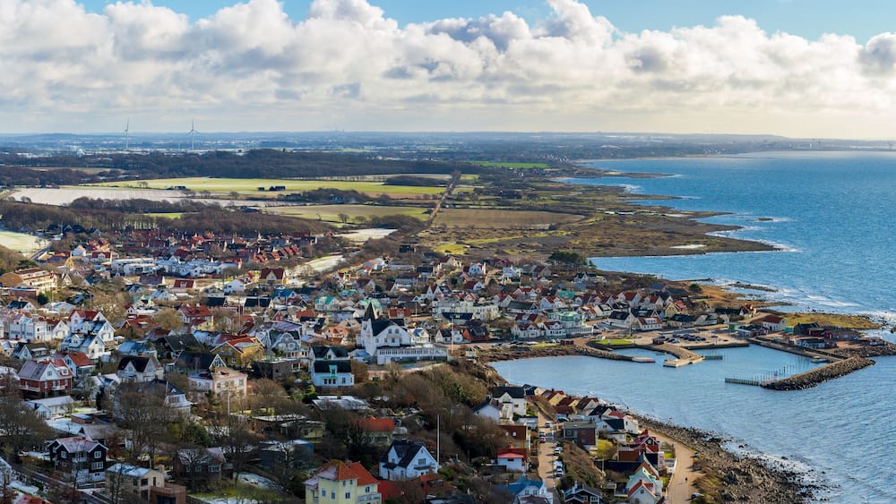 A coastal town with houses, a pier, and wind turbines in the distance.