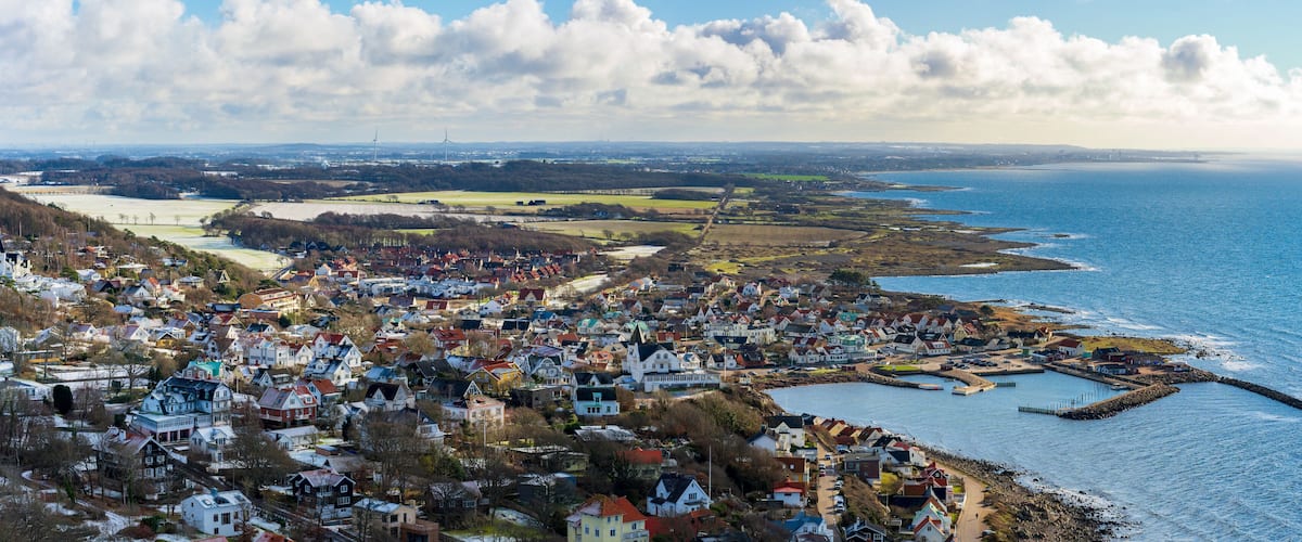 A coastal town with houses, a pier, and wind turbines in the distance.