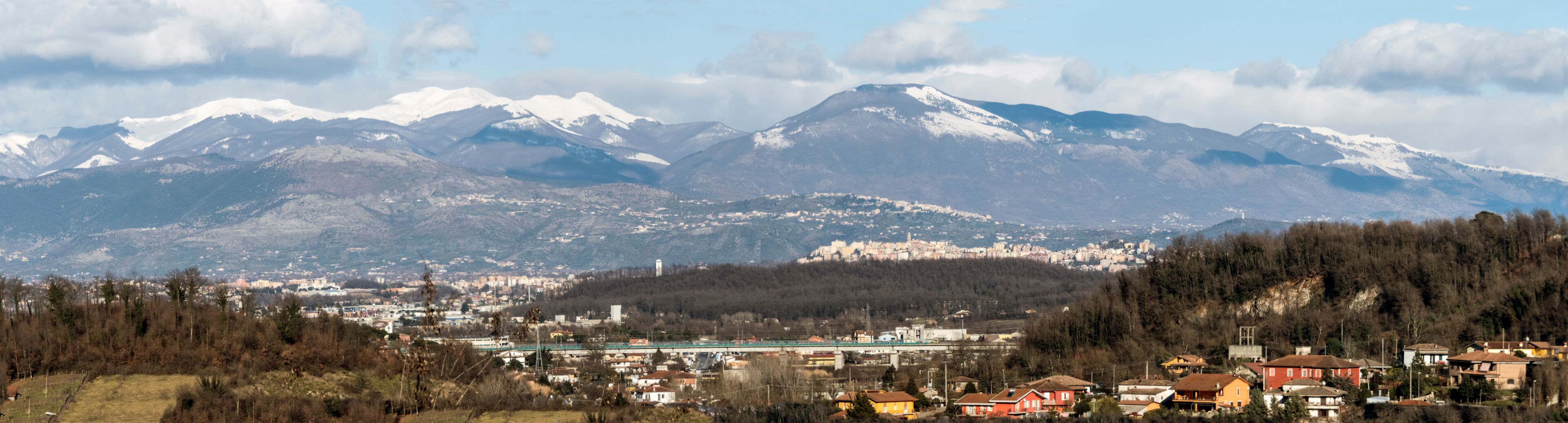 A town with snow-capped mountains in the background and a bridge in the foreground.