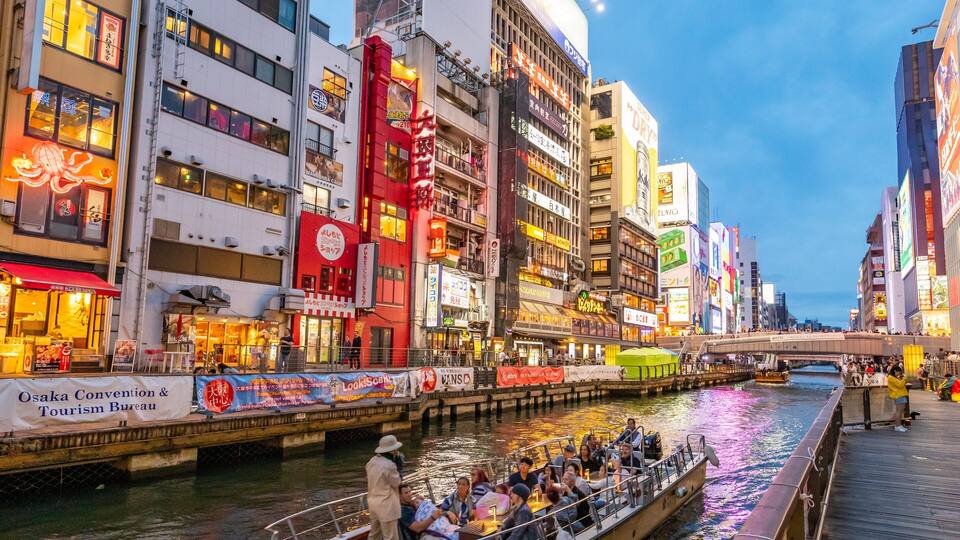 A bustling urban river scene with illuminated buildings and a boat tour.