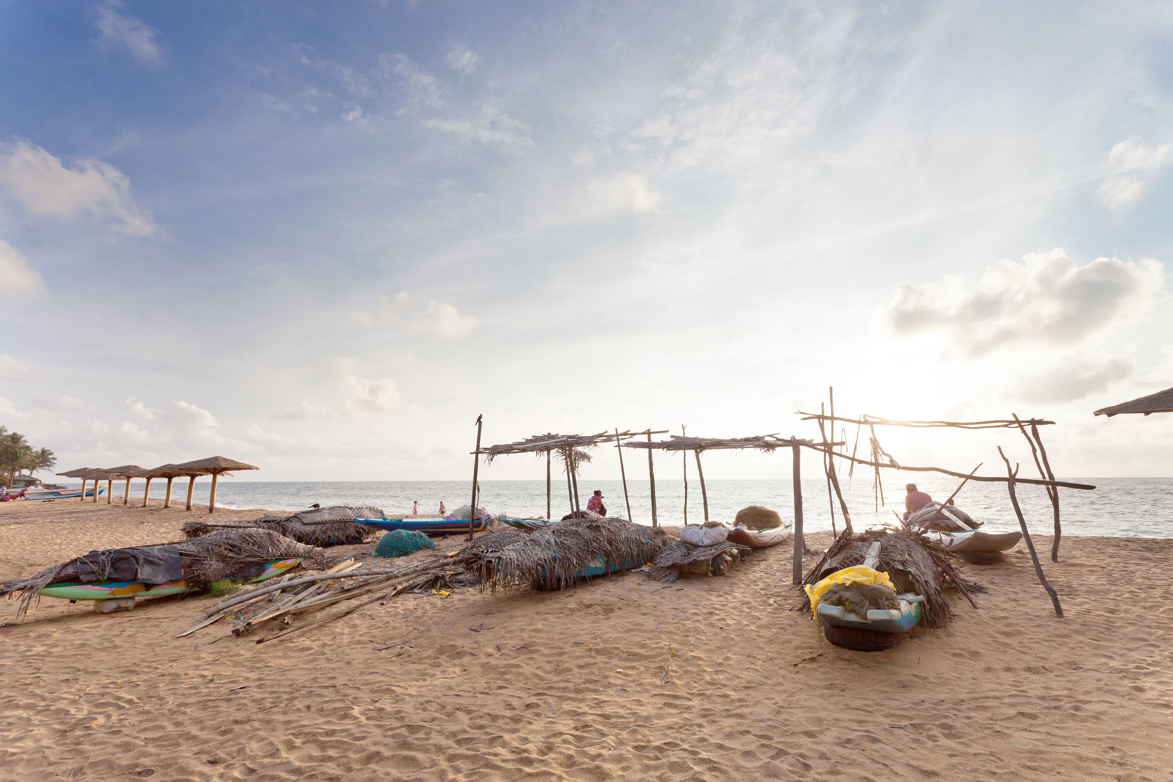 A beach with thatched huts, boats, and a calm sea.