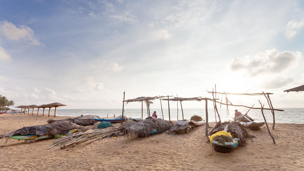 A beach with thatched huts, boats, and a calm sea.