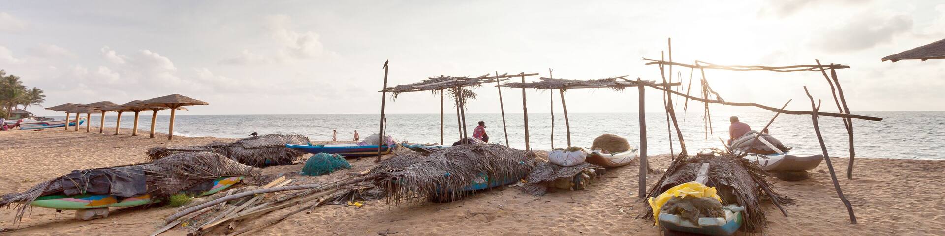 A beach with thatched huts, boats, and a calm sea.